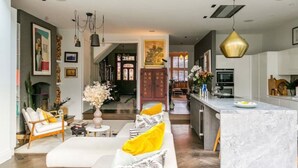 A modern living room with a sofa, a coffee table, and a dining area with a marble island. - Beautifully Curated 4 Bed Family Home w/ Garden (London)