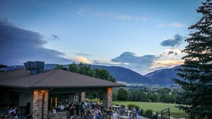 An outdoor patio area with stone pillars, tables, and chairs, overlooking a scenic landscape with mountains and a golf course. - Discover Year-Round Adventure at MH511 | Juniper Hollow Retreat in Eden, UT! (Eden)