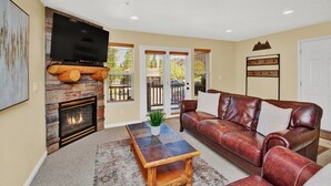 A living room with a fireplace, a television mounted on a stone wall, a brown leather sofa, and a coffee table. - Discover Year-Round Adventure at MH511 | Juniper Hollow Retreat in Eden, UT! (Eden)