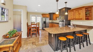 A modern kitchen with granite countertops, wooden cabinets, a central island with stools, and a dining area with a table and chairs. - Discover Year-Round Adventure at MH511 | Juniper Hollow Retreat in Eden, UT! (Eden)