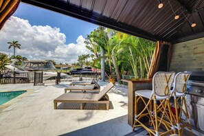 A covered outdoor area with lounge chairs, a barbecue grill, and a pool. - Pool & Home Theater: Lighthouse Point Home! (Lighthouse Point)