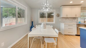 A modern kitchen with a white table, white chairs, a chandelier, and a view of the outdoors. - Boise Retreat ~ 2 Mi to Boise State University! (Boise)