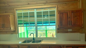 A kitchen with wooden cabinets, a double sink, and a window with a view of a balcony. - Presidential Suite Cottage 10 (Pointe Michel)