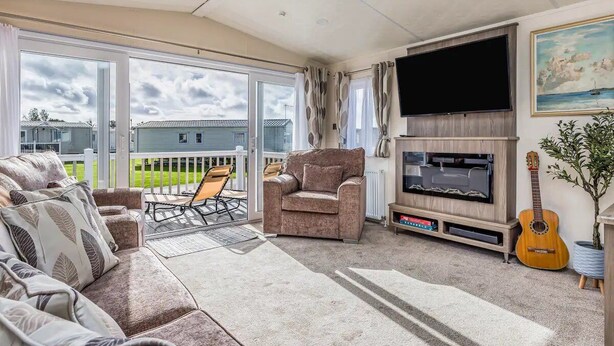 Ein geräumiges Wohnzimmer mit großem Fernseher, bequemen Sitzmöglichkeiten, einer Gitarre und einem Balkon mit Blick auf Häuser.