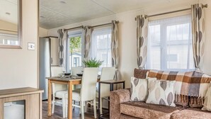 Ein gemütliches Wohnzimmer mit einer Couch, einem Esstisch und Stühlen. Ein Fenster mit Vorhängen bietet einen Blick ins Freie.