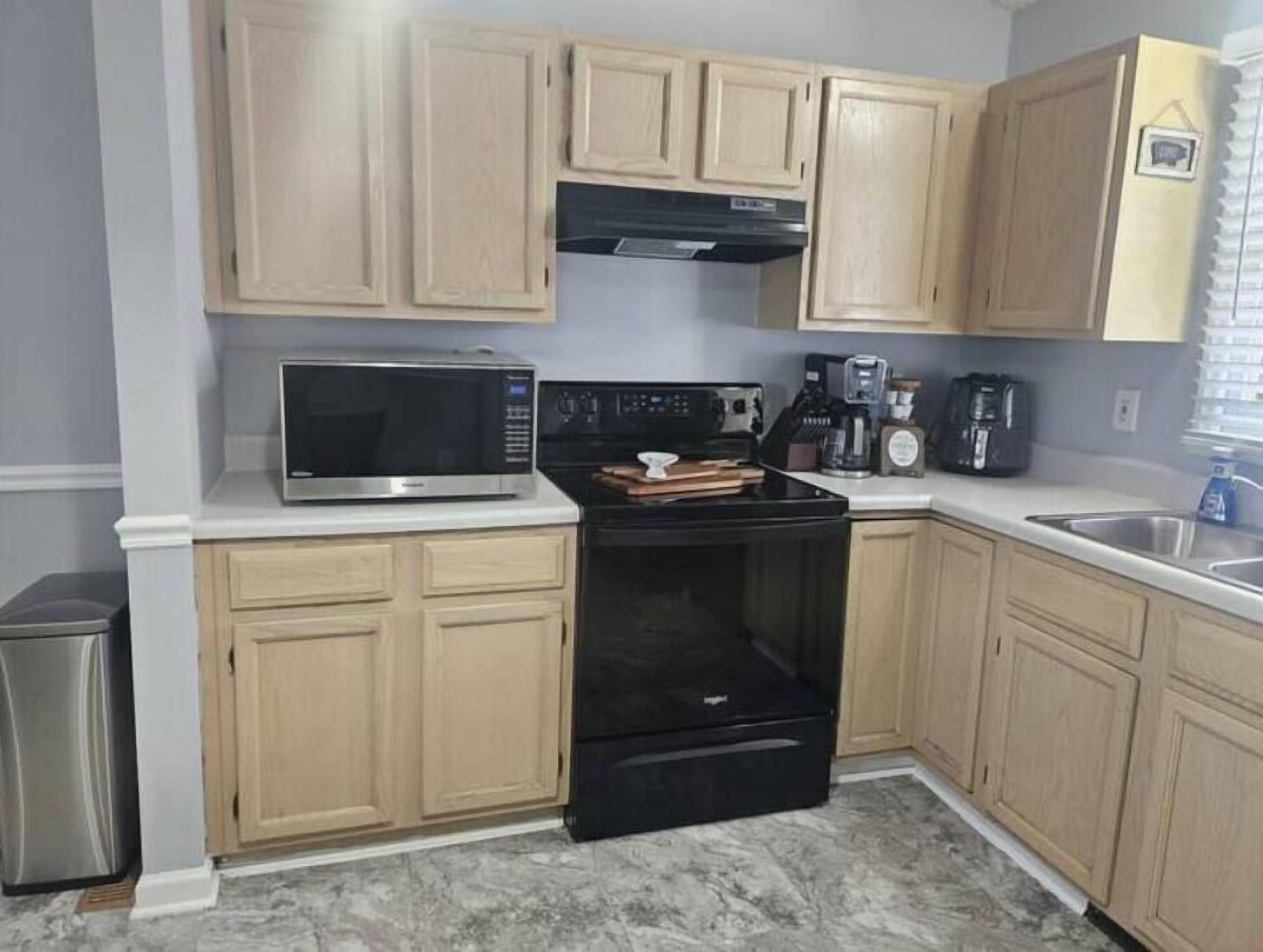 Cucina con mobili chiari in legno, un forno a microonde in acciaio inossidabile, un piano cottura nero e una macchina da caffè.
