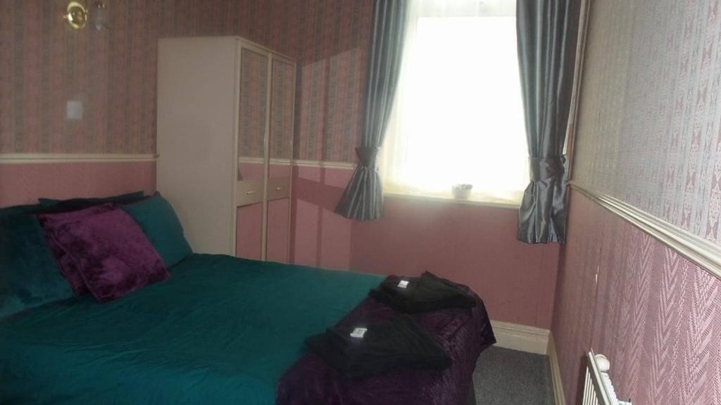 A bedroom with a bed, a wardrobe, and a window with curtains.