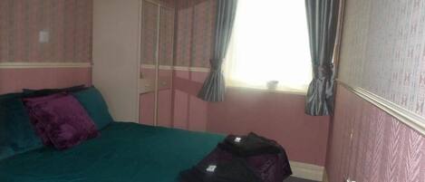 A bedroom with a bed, a wardrobe, and a window with curtains.