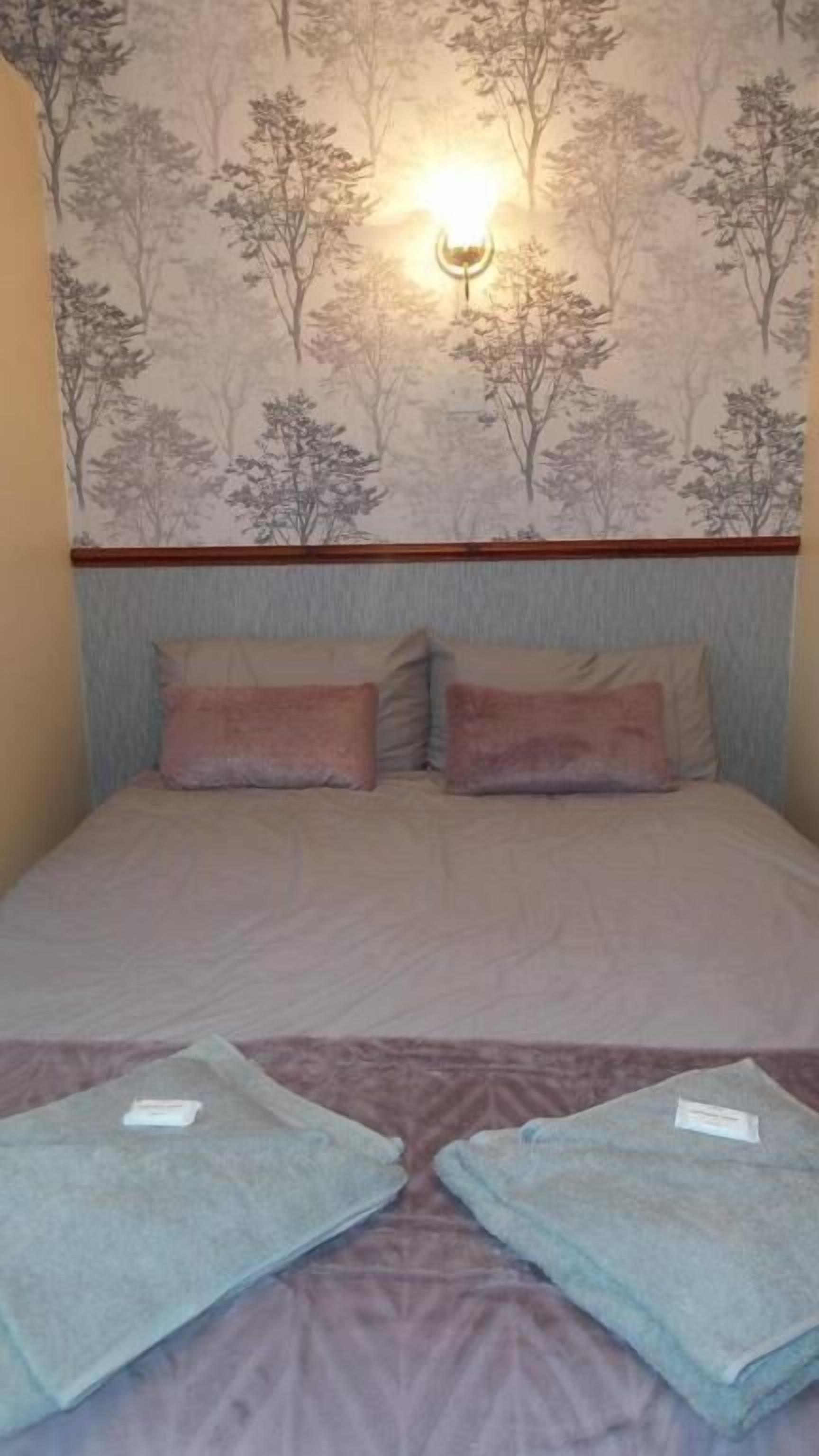 Une chambre d’hôtel avec un lit, deux oreillers, une tête de lit et un mur orné d’un motif représentant un arbre. Il y a deux serviettes sur le lit.