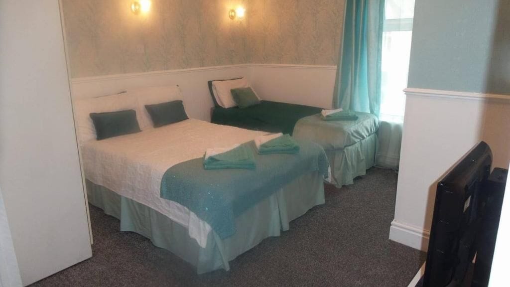 Une chambre d’hôtel avec deux lits simples, une télévision et une fenêtre avec des rideaux.