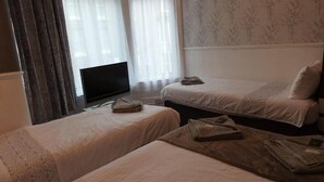 Ein Hotelzimmer mit zwei Einzelbetten, einem Fernseher und einem Fenster mit durchsichtigen Vorhängen.