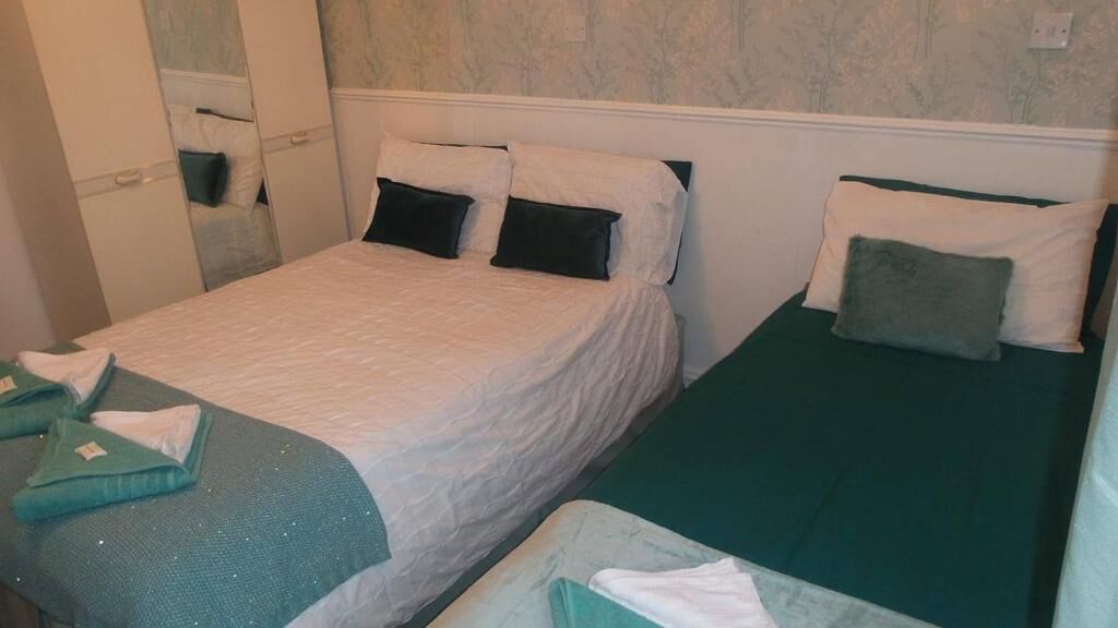 A room with two single beds, each with a green bedspread and white pillows. There is a small table with a green cloth and a folded towel.