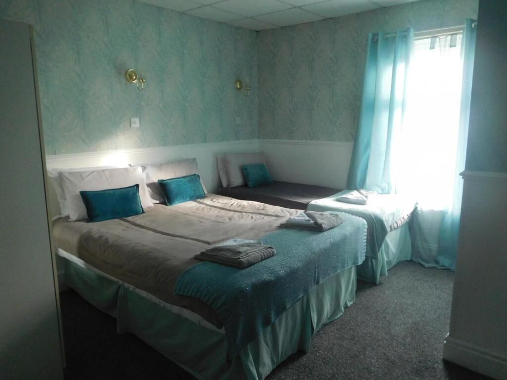 Une chambre avec deux lits, une fenêtre avec des rideaux et un luminaire fixé au mur.