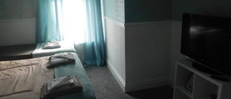 Una habitación de hotel con una cama, un televisor sobre un mueble y una ventana con cortinas.