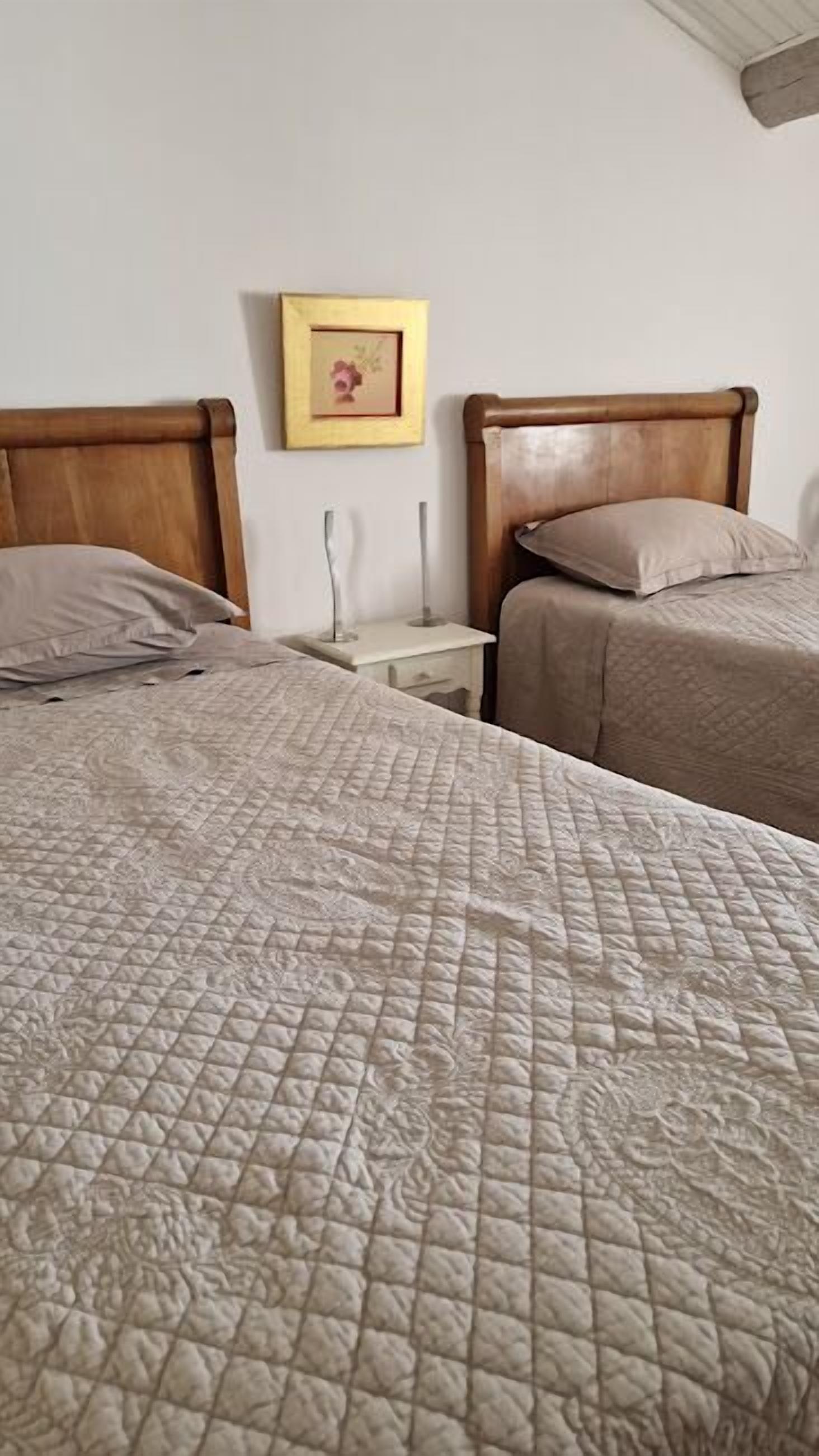 A bedroom with two beds, each with a wooden headboard, a bedside table, and a framed picture on the wall.