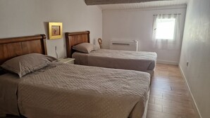A bedroom with two beds, a bedside table, a wall-mounted air conditioner, and a window with sheer curtains. - Art, Sailing, Fishing, Beach ... Sérignan! (Sérignan)