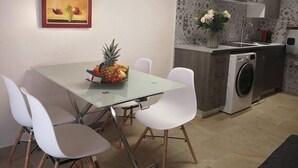 A compact kitchen with a dining area, featuring a glass table, white chairs, a washing machine, and a decorative wall piece. - Art, Sailing, Fishing, Beach ... Sérignan! (Sérignan)
