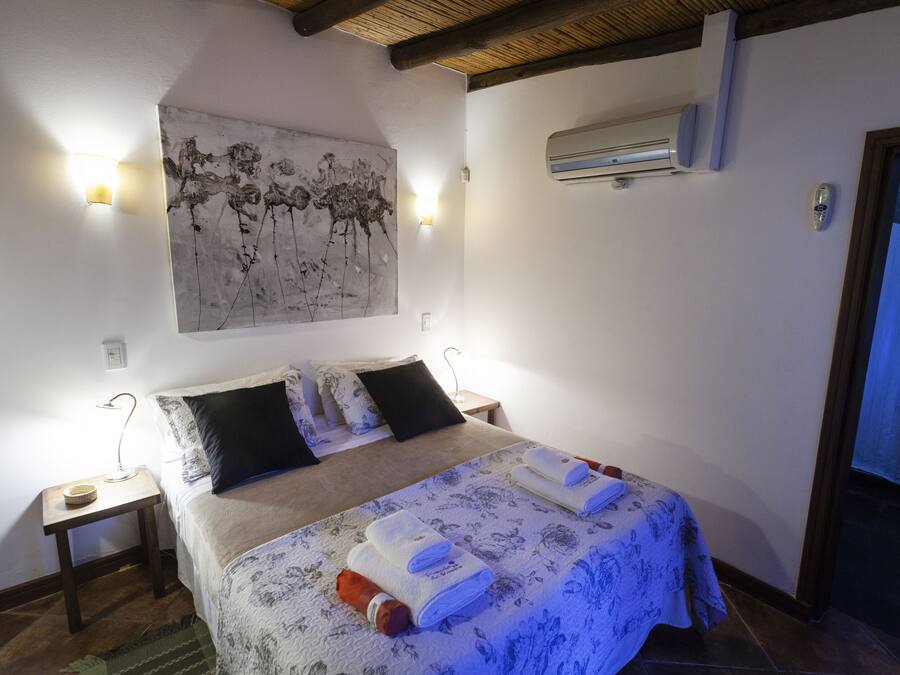 Un dormitorio con una cama, una mesita de noche, un aire acondicionado instalado en la pared y un cuadro.