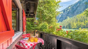 A balcony with a checkered tablecloth, red chairs, and a table set with a bottle, a glass, and a plate. - Le Petit Rêve - Lac de Montriond (Montriond)