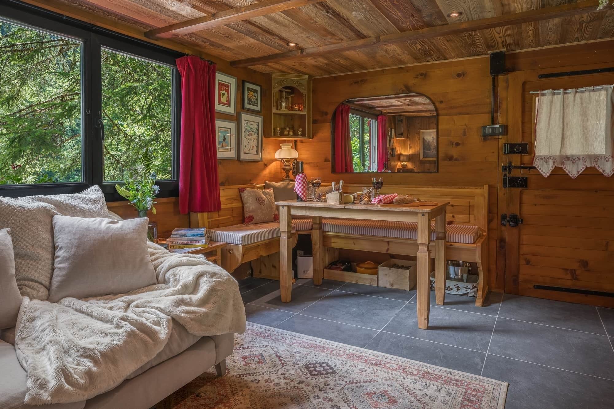 L'interno accogliente di una baita con un divano, un tavolo da pranzo in legno, uno specchio e una finestra con una tenda rossa.