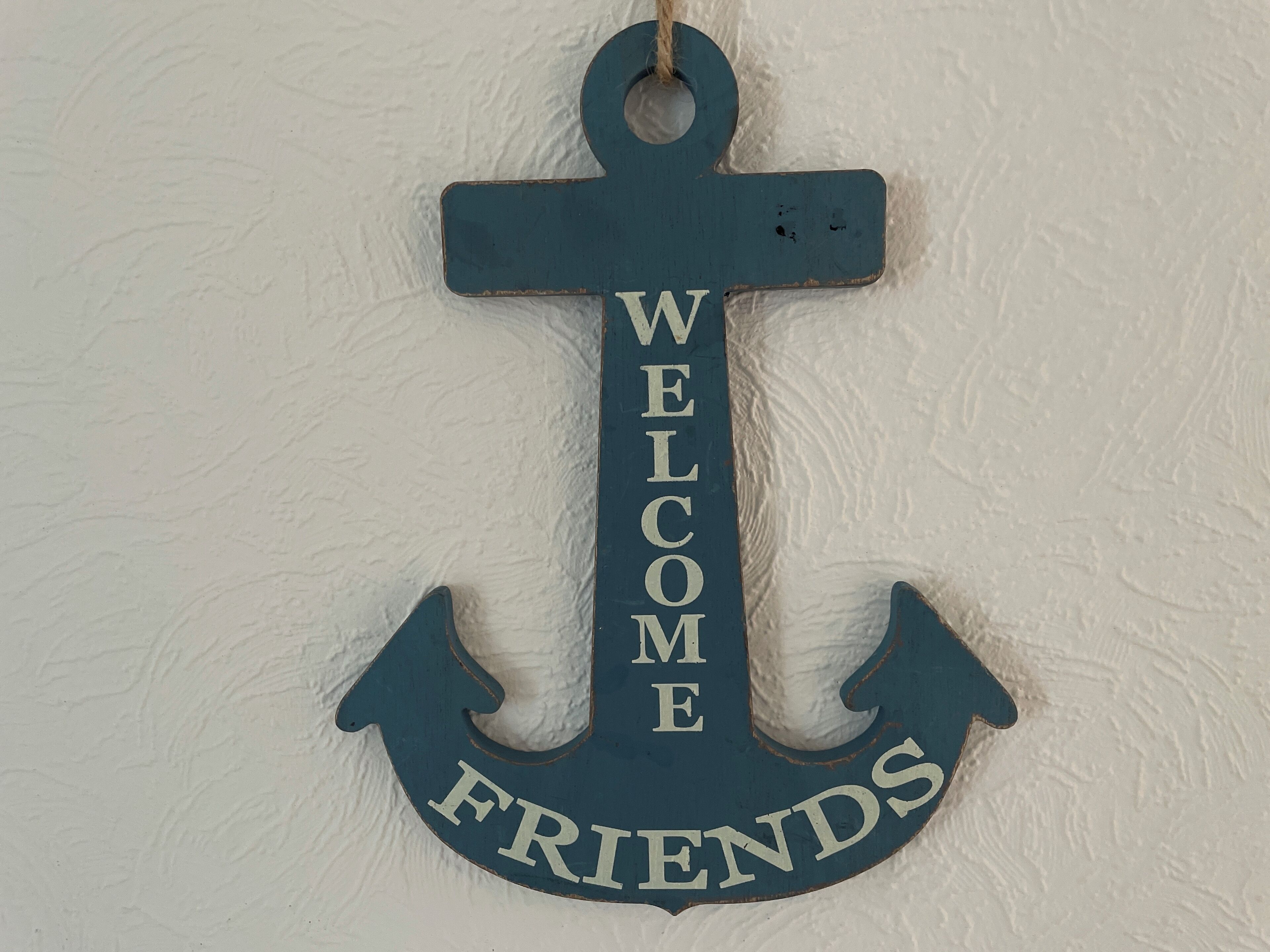 A wooden anchor-shaped sign with the words "WELCOME FRIENDS" on a textured wall.