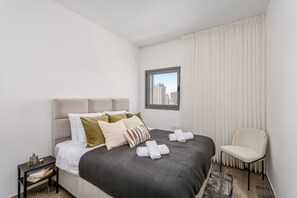 A hotel room with a bed, a nightstand, a chair, and a window with curtains.