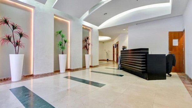 A modern hotel lobby with a reception desk, potted plants, and a curved ceiling design.
