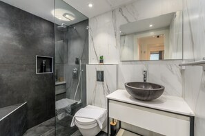 A modern bathroom with a glass-enclosed shower, a white toilet, a large marble sink, and a mirror above the sink. - City Center Apartment With Balcony in Jerusalem (Jerusalem)