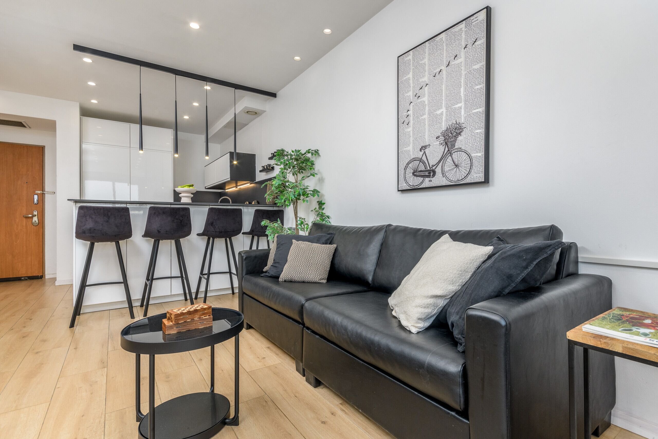 Una sala de estar moderna con un sofá de cuero negro, una mesita redonda y una zona de bar con taburetes.