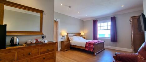 A hotel room with a wooden dresser, a bed with a headboard, a red leather chair, a large mirror, and a window with purple curtains.