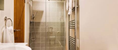 A modern bathroom with a glass-enclosed shower, a wooden floor, a white sink, and a towel rack.