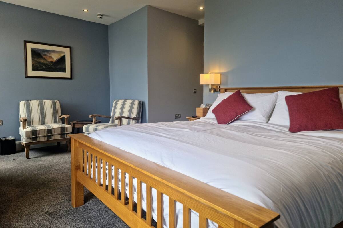 A hotel room with a large bed, two chairs, a nightstand, a lamp, and a painting on the wall.