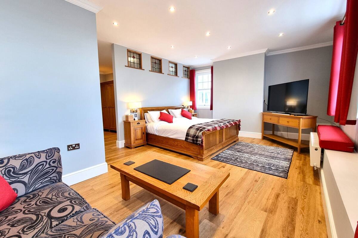 A bedroom with a bed, bedside tables, a TV, a sofa, and a coffee table.