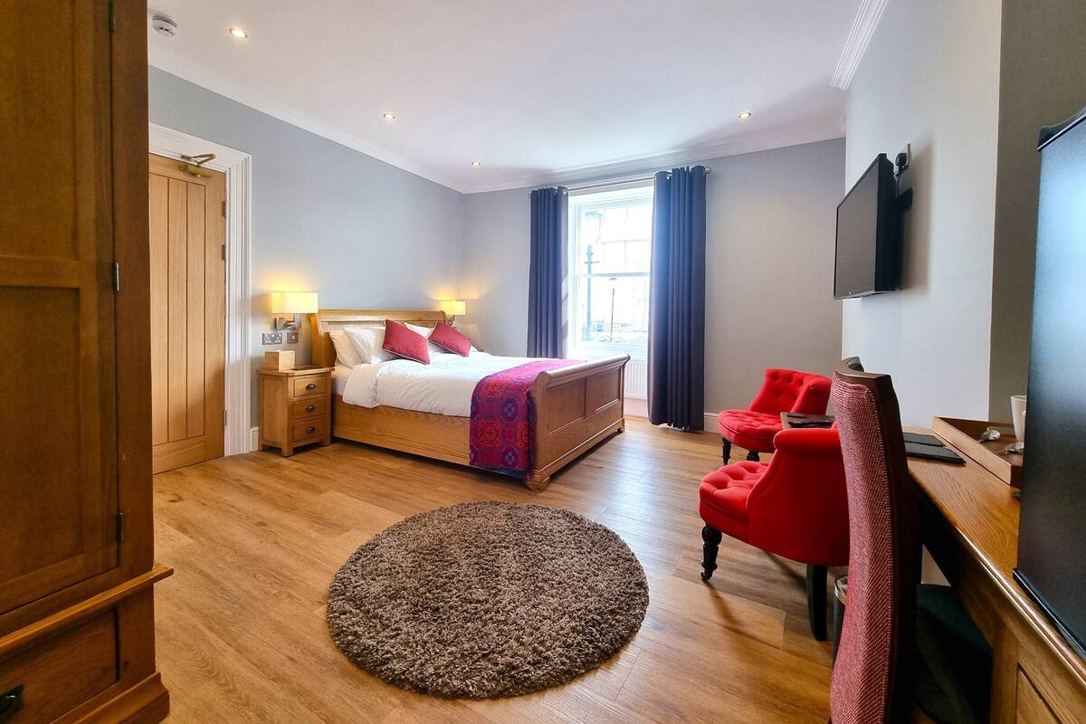 A hotel room with a bed, a desk, a chair, a TV, and a window with curtains.