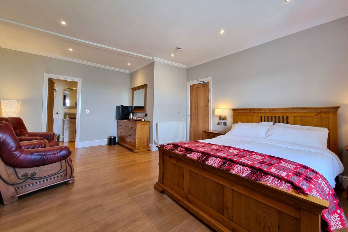 A bedroom with a wooden bed, a leather armchair, a dresser, and a mirror.