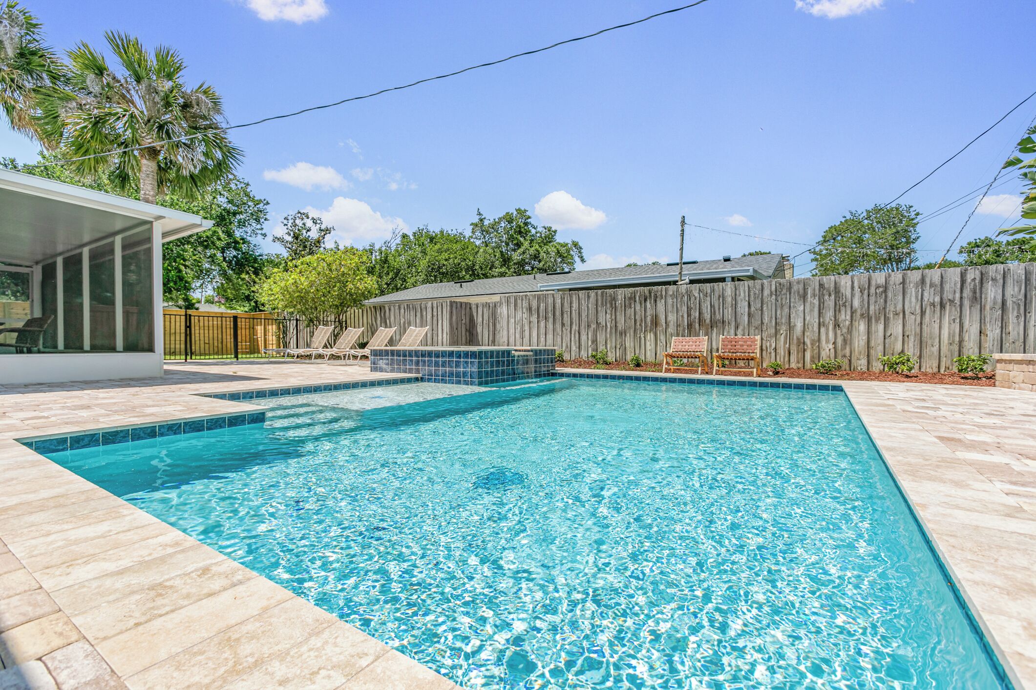 A rectangular swimming pool with clear blue water, surrounded by a wooden fence and a covered patio area.