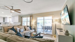 A spacious living room with a sofa, coffee table, and a ceiling fan. There is a sliding glass door leading to an outdoor patio area. - Summer Breeze - Pool and Heated Spa Near Amphitheatre, Historic Downtown, Beach (St. Augustine)