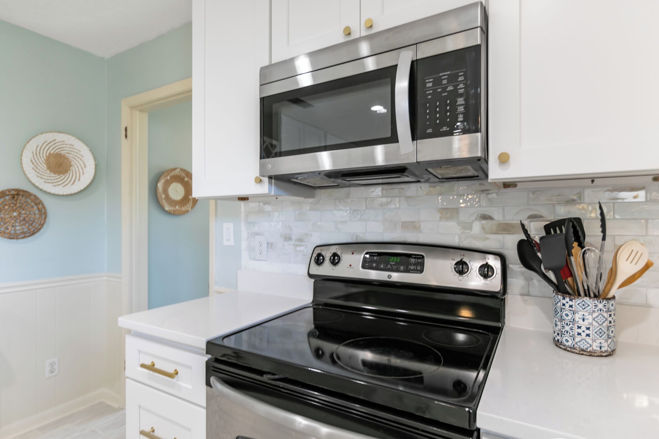 A kitchen with white cabinets, a stainless steel microwave, a black stove, and a tiled backsplash.