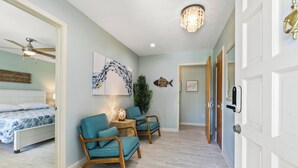 A bedroom with a bed, two chairs, a nightstand, and a wall-mounted fish decoration. - Summer Breeze - Pool and Heated Spa Near Amphitheatre, Historic Downtown, Beach (St. Augustine)