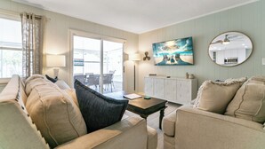 A living room with a sofa, armchairs, a coffee table, a painting, a mirror, and a view through a glass door. - Summer Breeze - Pool and Heated Spa Near Amphitheatre, Historic Downtown, Beach (St. Augustine)