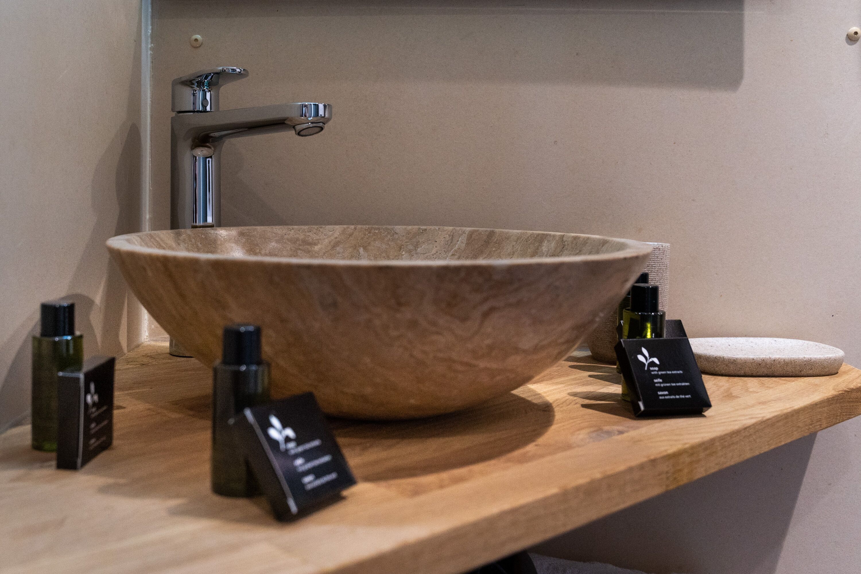 A wooden vanity with a large, oval-shaped vessel sink, a modern faucet, and several skincare products on the counter.