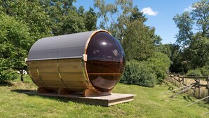 Een grote, cilindervormige constructie met een reflecterend oppervlak, geplaatst op een houten platform in een grasrijk gebied met bomen op de achtergrond.