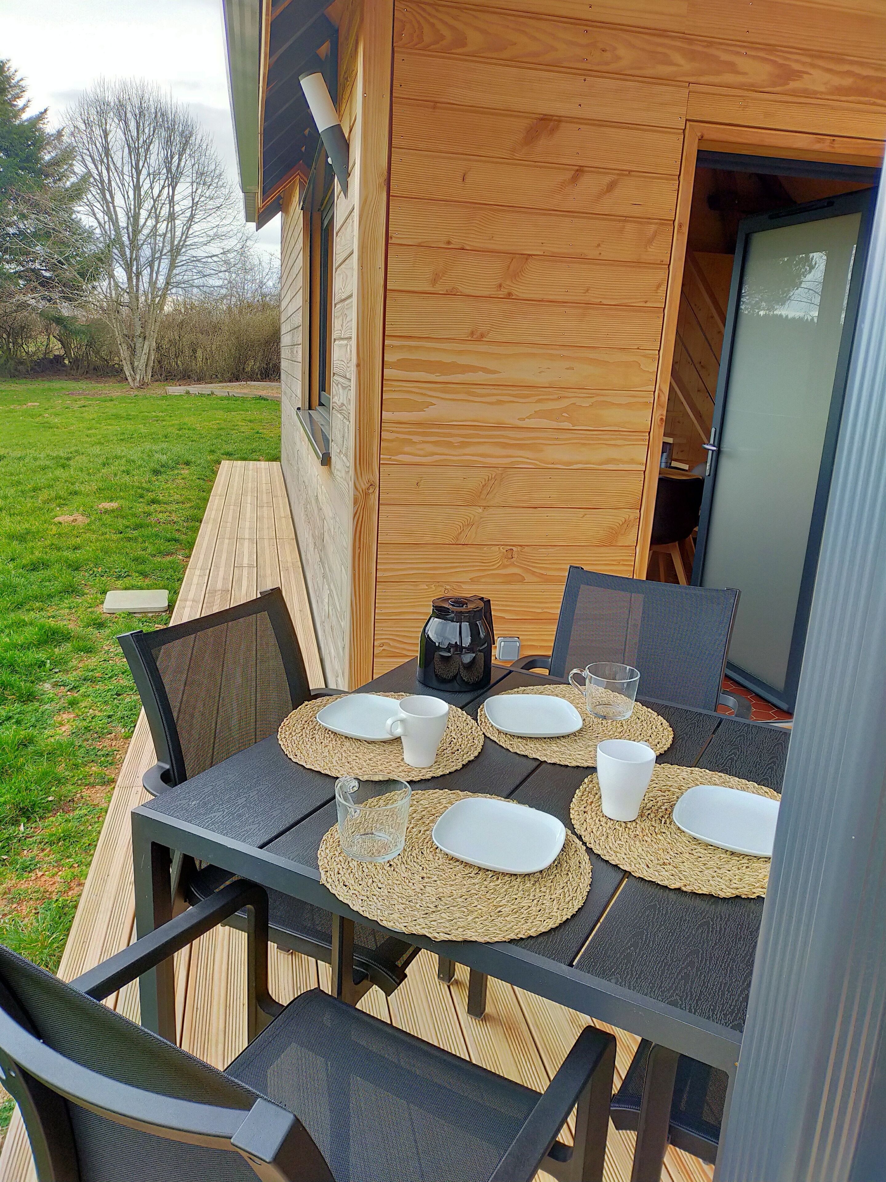 Ein Essbereich im Freien mit einer Holzterrasse, Tisch gedeckt mit Tellern, Tassen und einer Kaffeekanne.