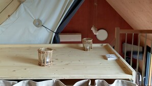 Een tent met een houten tafel, twee kandelaars en een witte gordijn.