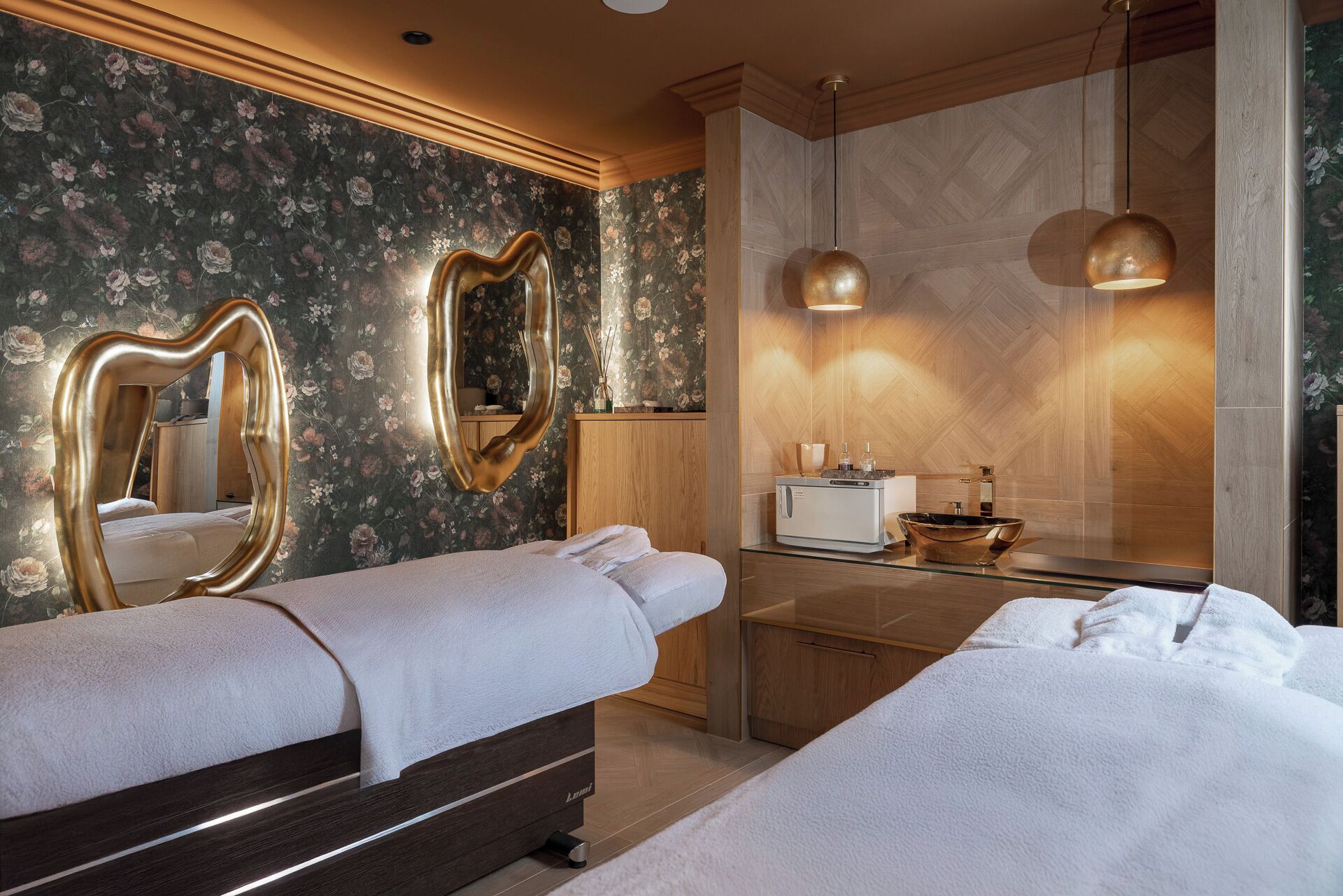 Quarto de hotel com duas camas, guarda-roupa de madeira, toucador com espelho e banheiro moderno com pia e espelho grande.
