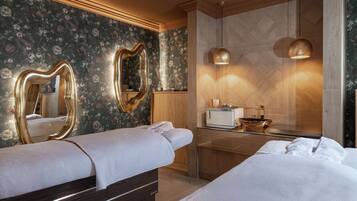 Quarto de hotel com duas camas, guarda-roupa de madeira, toucador com espelho e banheiro moderno com pia e espelho grande.