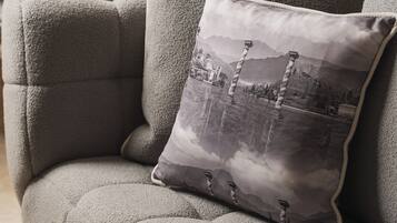 A grey upholstered sofa with a textured fabric and a decorative pillow featuring a monochrome landscape print.