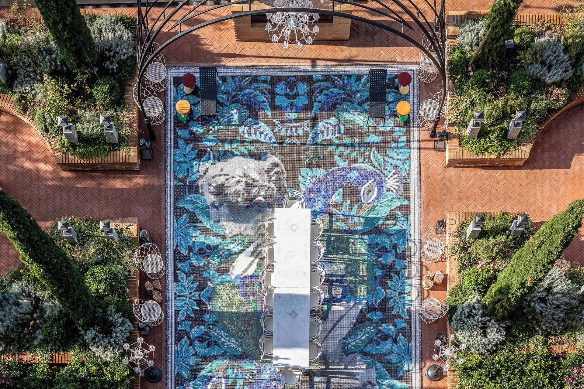 Vista aérea de una piscina en la azotea con diseño de mosaico, rodeada de follaje y mobiliario exterior.