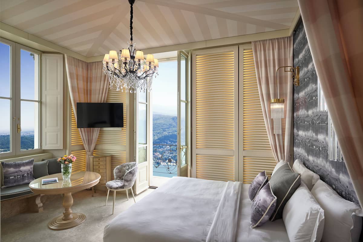 Un dormitorio amplio con una cama grande, televisión, candelabro y vistas a la ciudad.