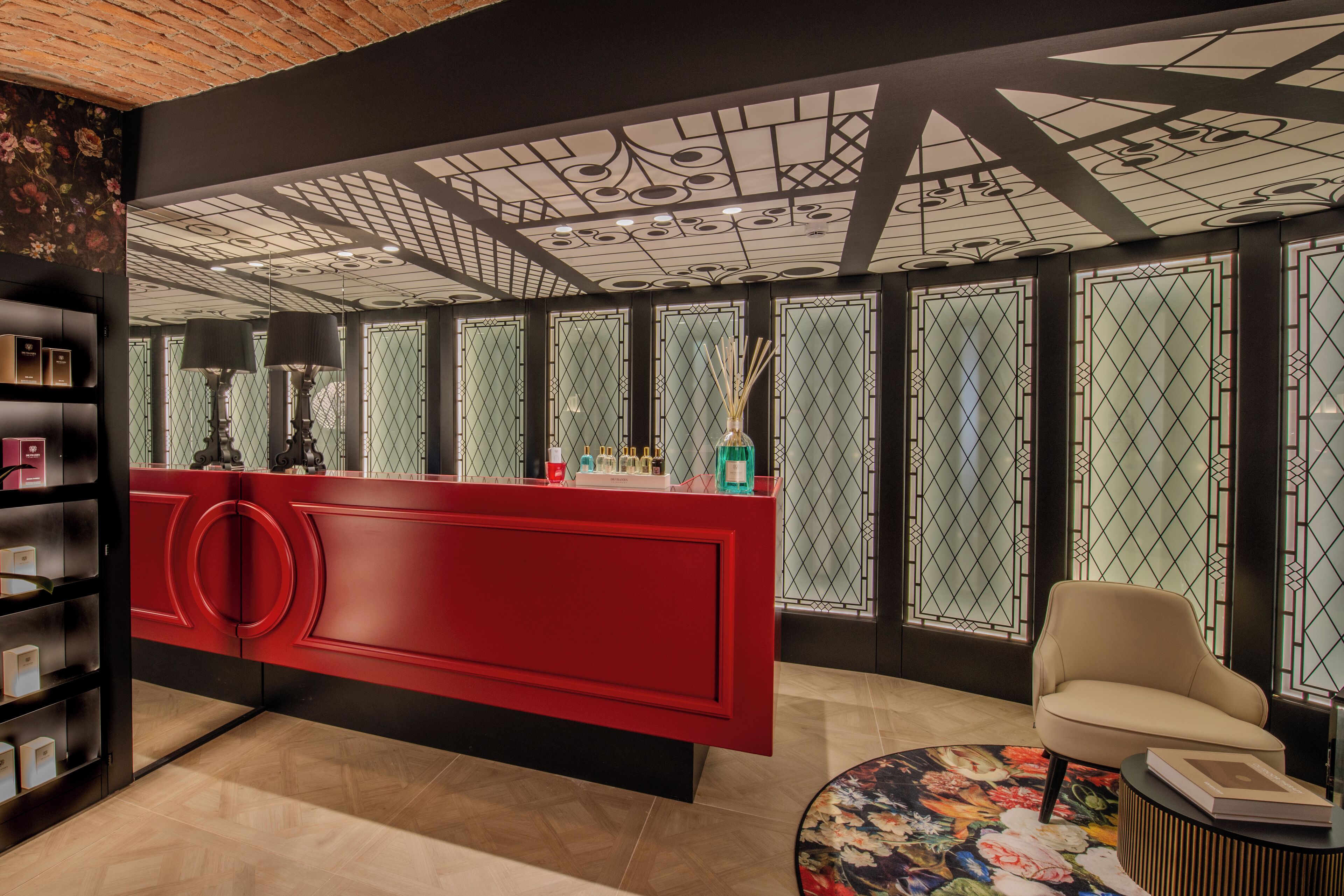 Un espace d’accueil moderne avec un bureau rouge, un fauteuil beige et un tapis à motifs floraux.